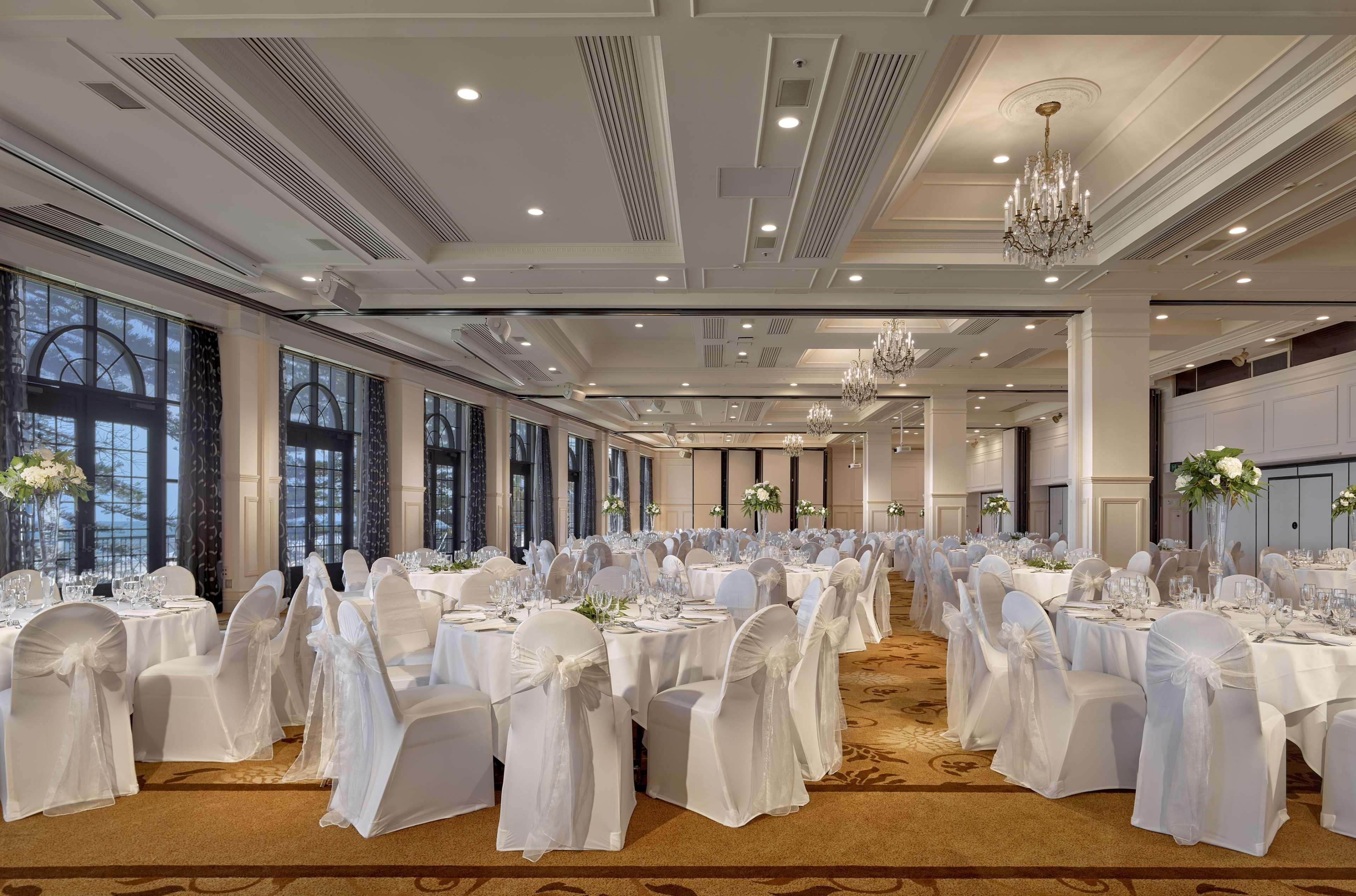 Stamford Grand Adelaide Hotel Glenelg Bagian luar foto The photo depicts an elegantly arranged banquet hall or dining area. The space features multiple round tables, each set with white tablecloths and decorated with floral centerpieces. The chairs are covered in white fabric, contributing to a formal at
