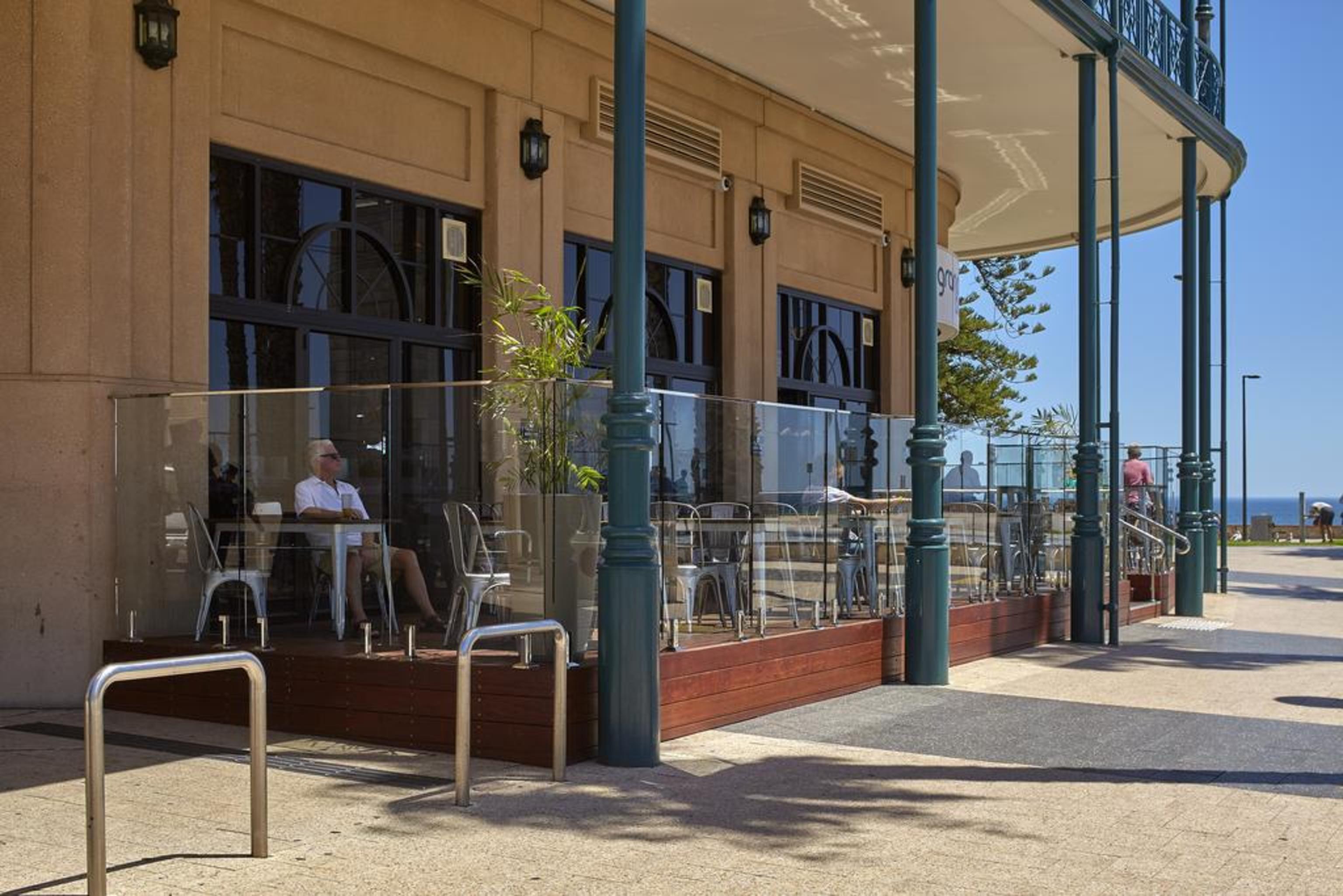 Stamford Grand Adelaide Hotel Glenelg Bagian luar foto The photo shows the exterior of a cafe or restaurant with a large outdoor seating area. There are glass barriers around the seating, providing a view of the outside while maintaining a sense of enclosure. The building has a modern architectural style