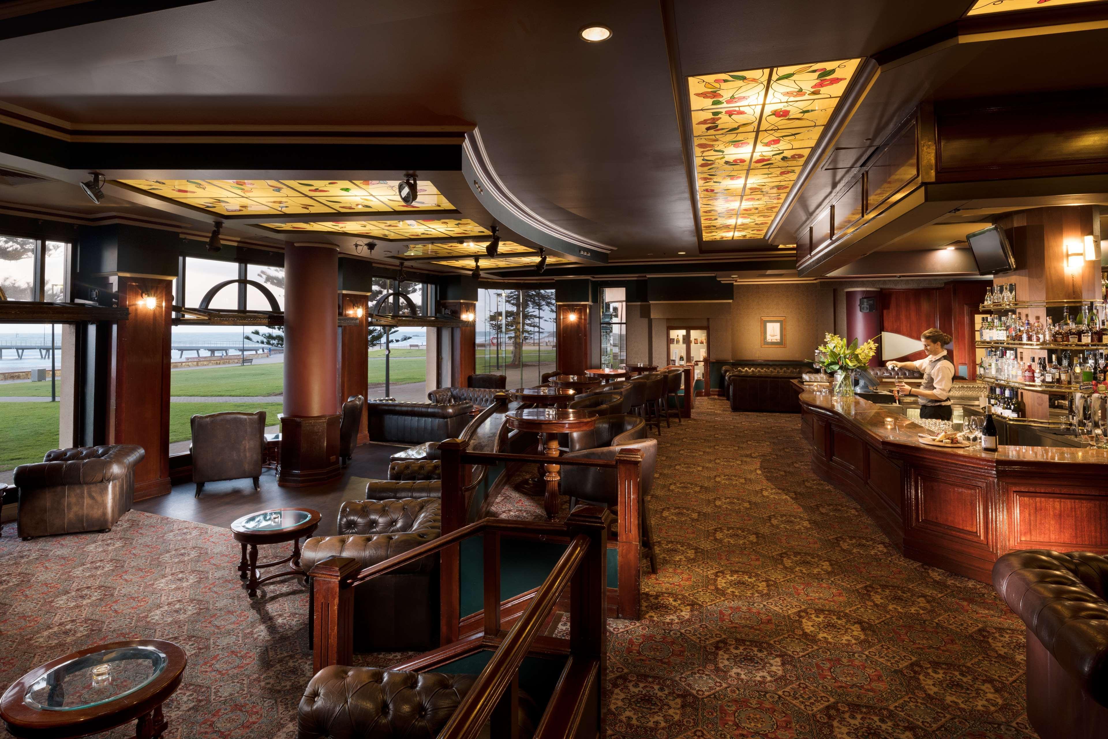Stamford Grand Adelaide Hotel Glenelg Bagian luar foto The photo depicts a stylish and upscale bar or lounge area. The interior features elegant wooden furniture, including plush chairs and tables. The ceiling is adorned with decorative elements, and the lighting provides a warm ambiance. A bar counter c