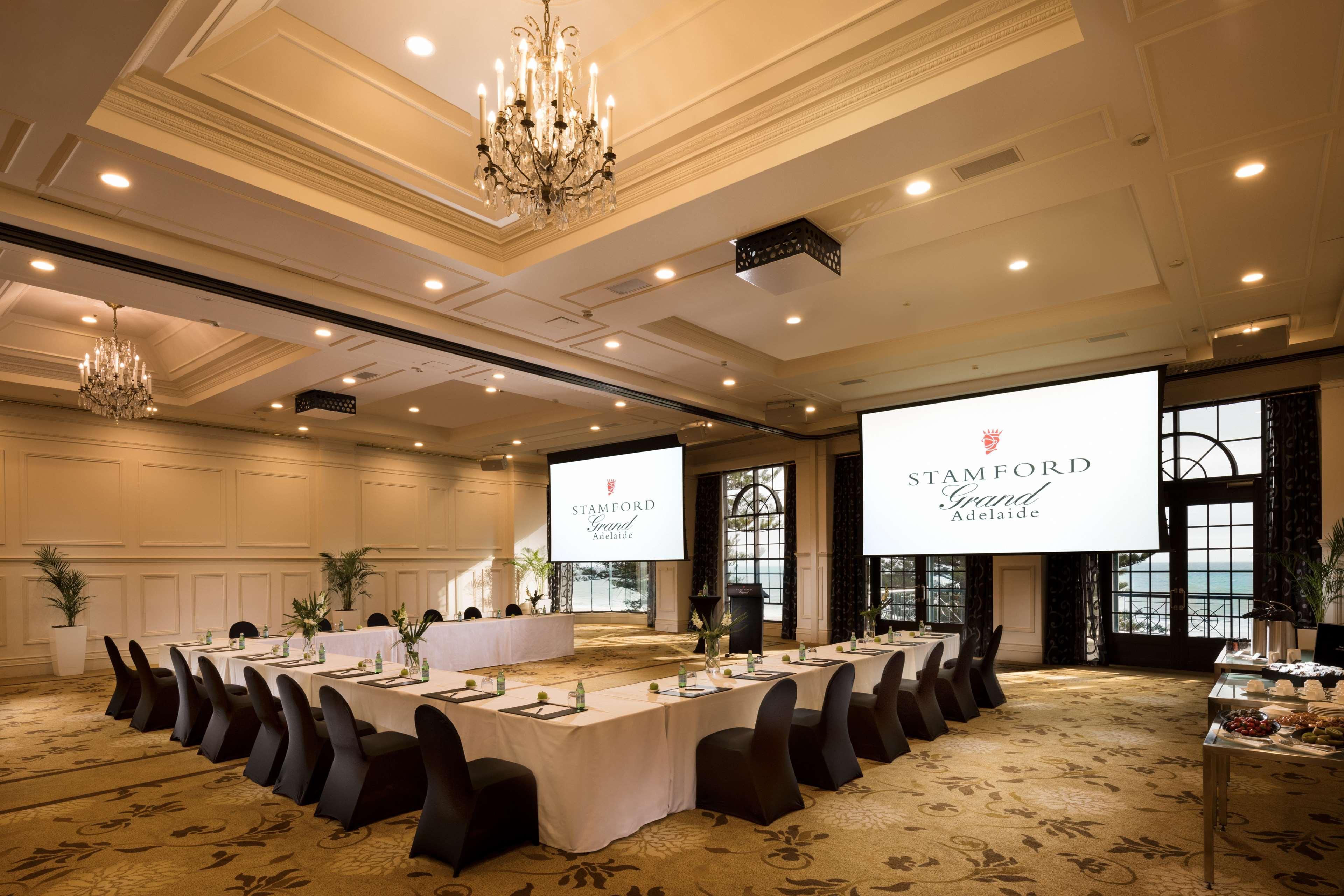 Stamford Grand Adelaide Hotel Glenelg Bagian luar foto The photo shows a spacious and elegantly designed conference room. The room features a long table set for a meeting, surrounded by stylish chairs. Two large screens are positioned at the front, displaying the logo "Stamford Grand Melbourne." The ceil