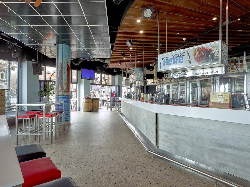 Stamford Grand Adelaide Hotel Glenelg Bagian luar foto The photo shows the interior of a modern bar or restaurant. The design features a long, white counter that serves as the bar area, with a glass display showing beverages. Behind the bar, there are shelves for drink storage. The space has a mix of sea