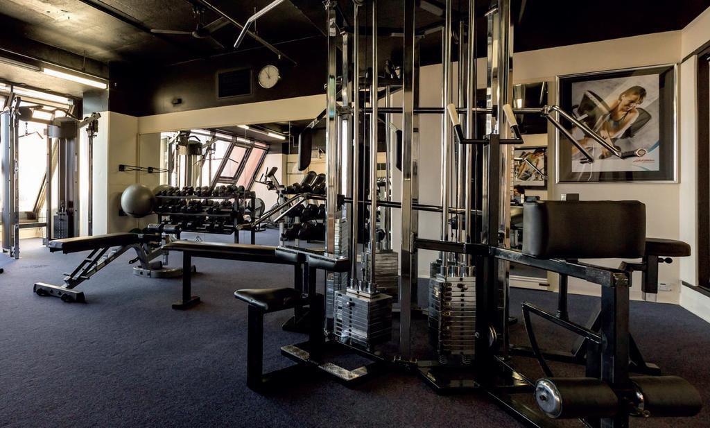 Stamford Grand Adelaide Hotel Glenelg Bagian luar foto The photo shows a gym interior with several pieces of exercise equipment. In the foreground, there is a multi-station machine that features various pulleys and weights. To the side, there are benches and free weights, including dumbbells. The gym has