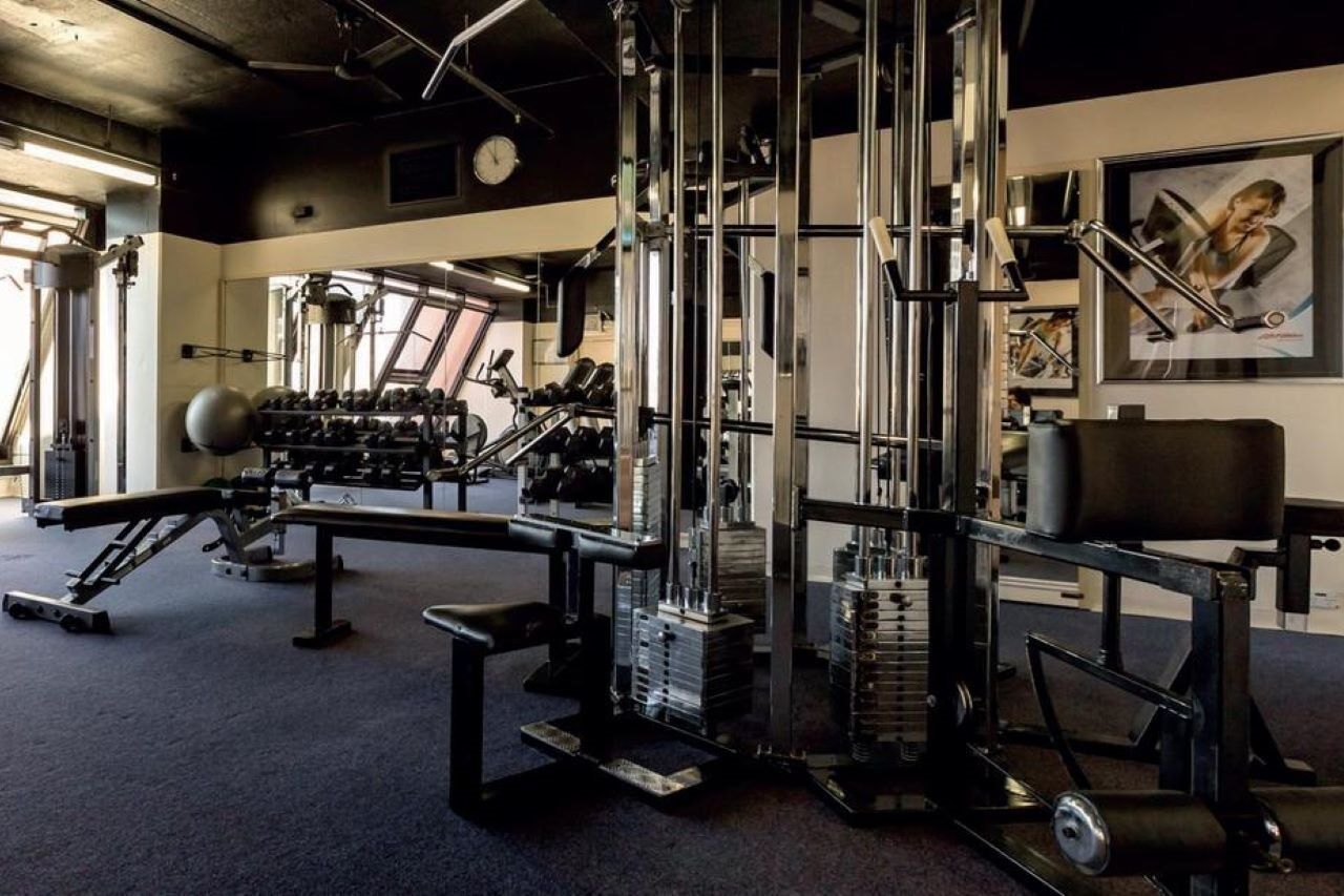 Stamford Grand Adelaide Hotel Glenelg Bagian luar foto The photo shows a gym interior with various exercise equipment. In the foreground, there is a multi-station cable machine, which has several adjustable weights and pulleys for a variety of strength training exercises. To the side, there's a bench and